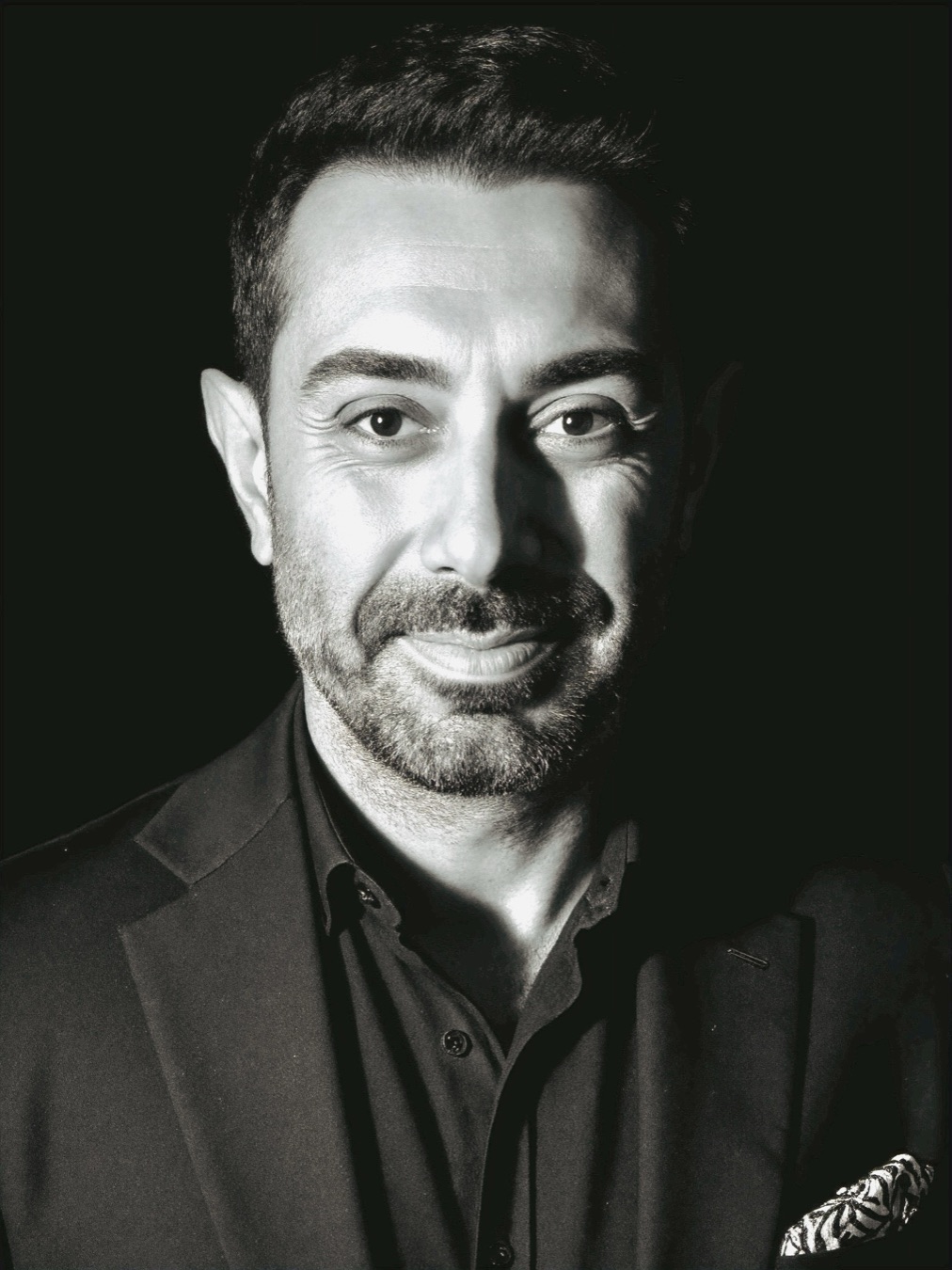 Black-and-white portrait of Emrah Olgac, smiling softly